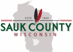 Logo for Sauk County, Wisconsin. The text ‘Sauk County’ appears in large green letters with red accents, and the word ‘Wisconsin’ is written below in red.
                        Two feathers, one black and one red, appear above the text along with ‘ESTD 1844.’ The background features a light gray silhouette of the state of Wisconsin.